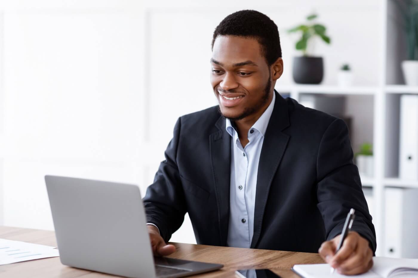 Security professional smiling while working on a laptop and taking notes