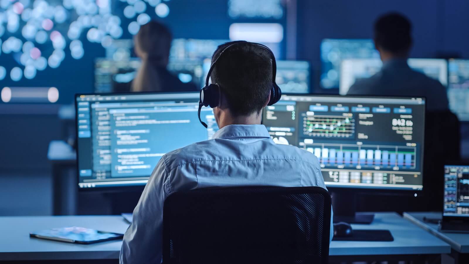 Security professional monitoring compliance data across multiple screens in an operations center